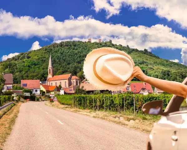 En bilresa längs den tyska rivieran, med en hatt som vinkar i vinden. En pittoresk by med en kyrka och vingårdar i bakgrunden.