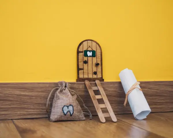 Puerta de madera para hacerla del ratoncito pérez, con una bolsa de dientes y un pergamino.