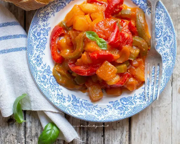 Un piatto di peperonata con patate, colorata e saporita, guarnita con basilico fresco.