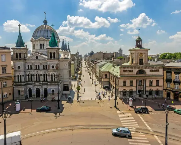 Widok na ulicę Piotrowską w Łodzi, z kościołem św. Stanisława Kostki i kamienicami. Tętniące życiem łódzkie stare miasto w słoneczny dzień.
