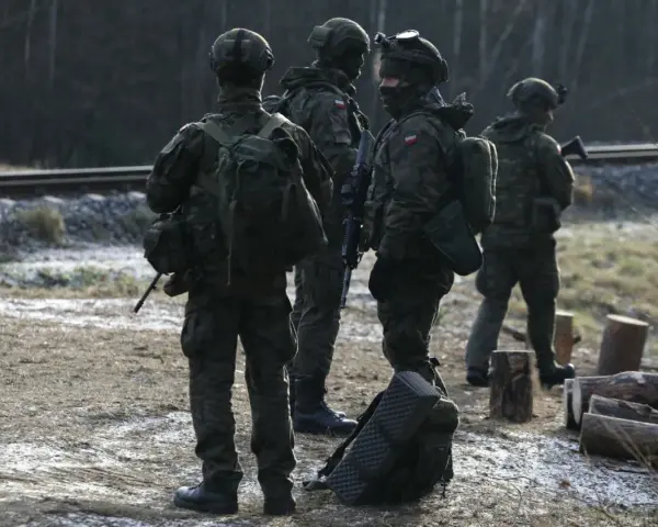 Szeregowi w wojsku patrolują teren przy torach kolejowych, gotowi do akcji.