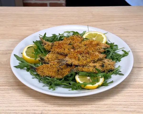 Piatto di alici al forno dorate e croccanti, servite su un letto di rucola fresca con spicchi di limone.