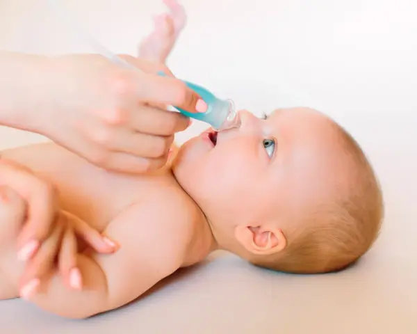 Manos cuidadosas realizan lavado nasal a un bebé.