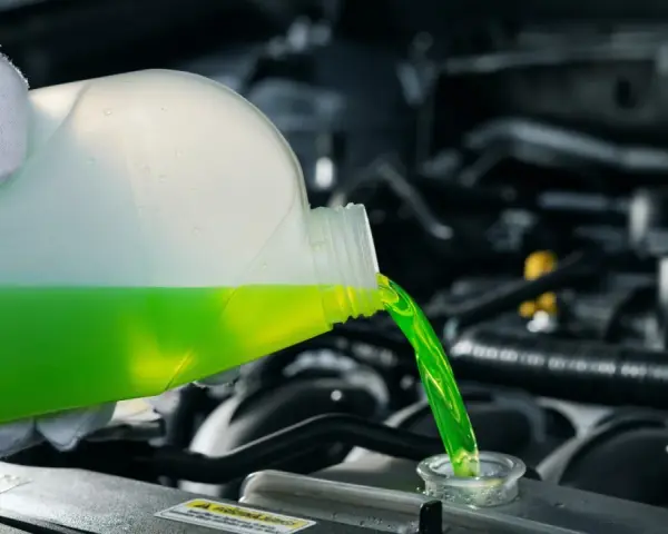 A gloved hand pours green antifreeze and coolant into a car's engine.