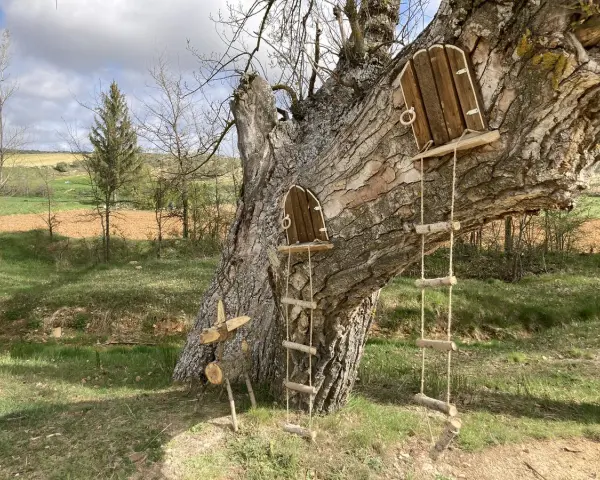 Un árbol con dos pequeñas puertas de madera y escaleras de cuerda, invitando a un arbolón paseo mágico. Un ciervo de madera decora la base.