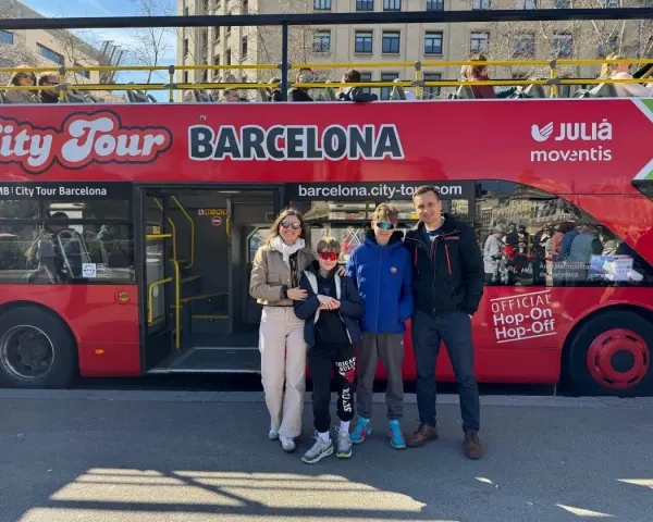 Family posing in front of a red "City Tour Barcelona" bus, ready for an adventure.