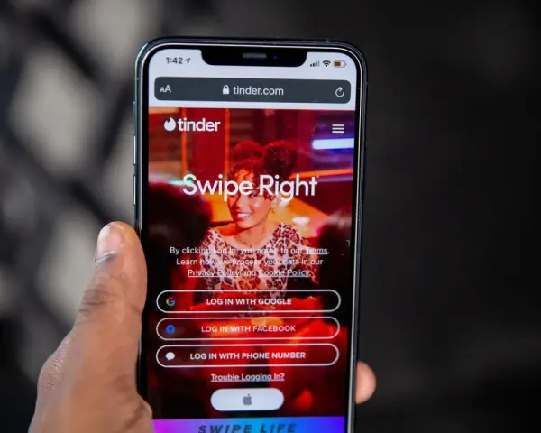Dłoń trzyma smartfon z otwartą stroną logowania portalu randkowego Tinder. "Swipe Right" zachęca do rozpoczęcia poszukiwań.