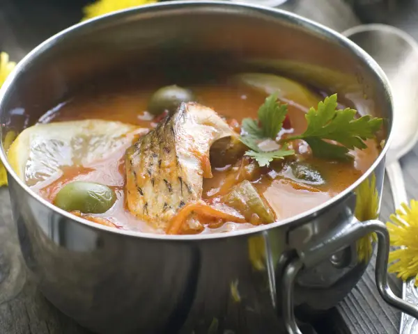 Aromaticzna rosyjska zupa rybna w metalowej misce, z kawałkami ryby, oliwkami, cytryną i natką pietruszki.