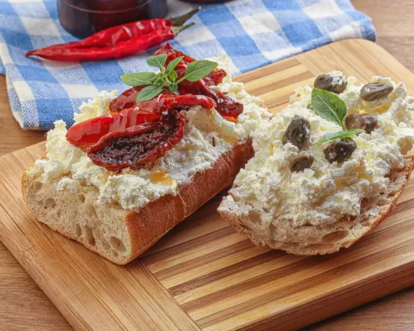 Dwa kawałki bagietki z twarogiem, suszonymi pomidorami i kaparami. Kapary dodają wyrazistego smaku, świetnie komponując się z serem i pomidorami.