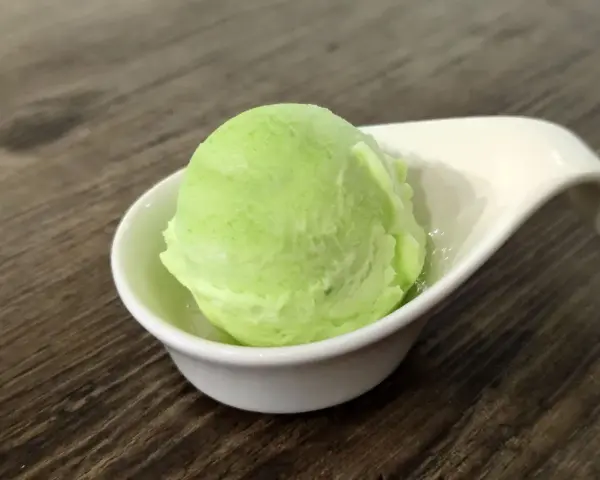 Una bola de helado de manzana verde brillante en una taza blanca sobre una mesa de madera.