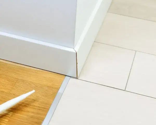 Precyzyjne łączenie płytek z panelami podłogowymi, biała listwa przypodłogowa i dysza z silikonem.