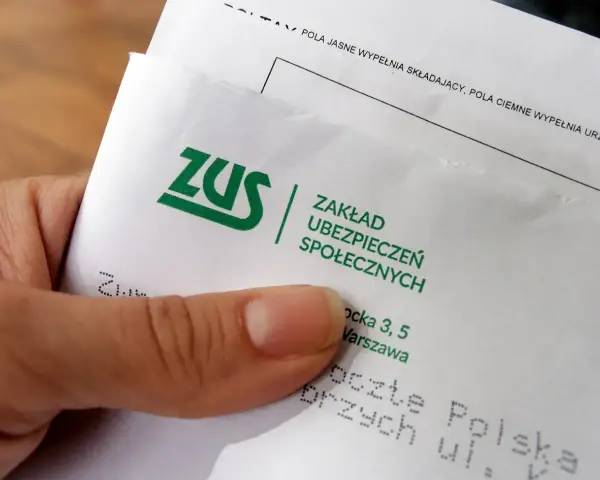 Dłoń trzyma dokument z logo ZUS i napisem "Zakład Ubezpieczeń Społecznych".
