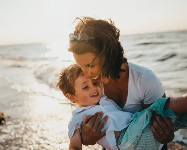 Ciepły moment na plaży, kiedy dziecko daje buziaka mamie. Słońce odbija się w falach.