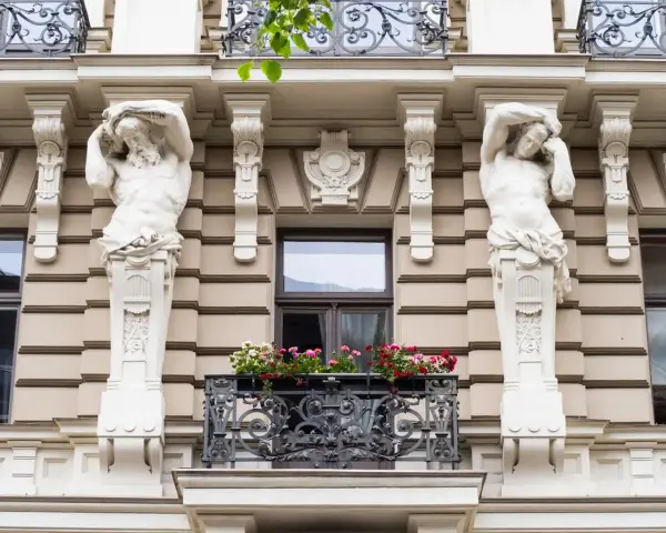 Dwie rzeźby atlantesów podtrzymujące balkon, przykład secesji w sztuce, zdobią fasadę kamienicy.
