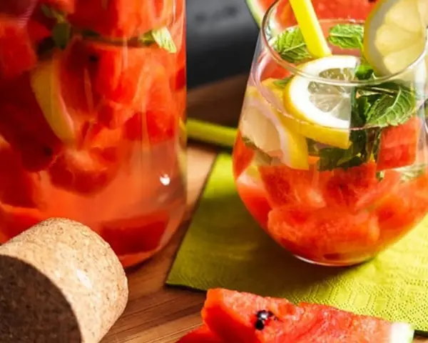 Orzeźwiający drink w arbuzie z cytryną i miętą, podany w szklance i karafce. Idealny na upalne dni.