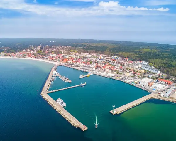 Widok z lotu ptaka na malowniczy hel port z licznymi łodziami i statkami. W tle rozciąga się miasto i las.