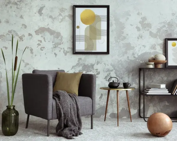 Salón moderno con pared texturizada que combina papel pintado y pintura. Sillón gris, mesa auxiliar dorada, plantas y arte abstracto.