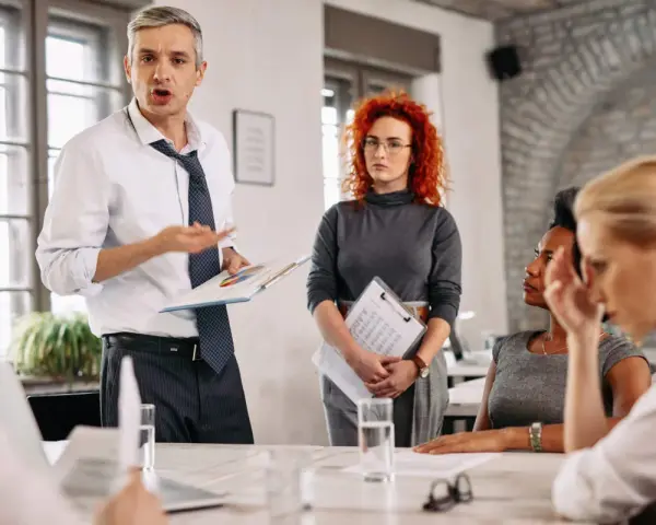 Un homme présente un rapport du liquidateur à une équipe. Une femme aux cheveux roux écoute attentivement.