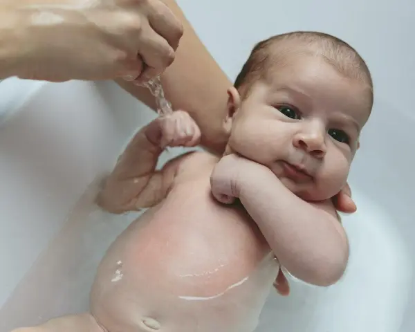 Niemowlę w wannie, delikatnie kąpane. Widoczny wypukły pępek maluszka.