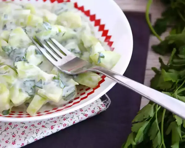 Ensalada cremosa de pepino y yogur con hierbas frescas en un plato blanco con borde rojo.