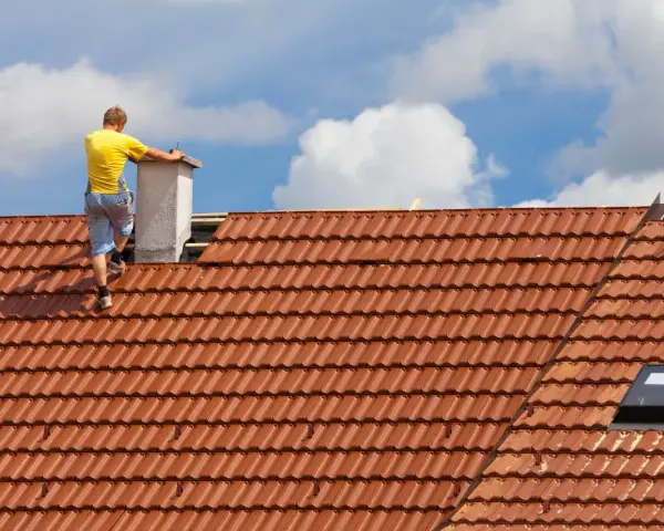 Pracownik na dachu buduje komin systemowy. Sprawdź, jaka jest murowanie komina systemowego cena robocizny.