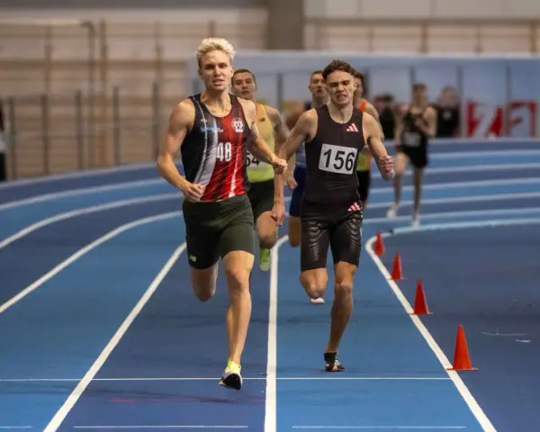Filip Ostrowski biegnie w zawodach lekkoatletycznych. Dwóch zawodników na pierwszym planie, jeden z numerem 48, drugi z 156.