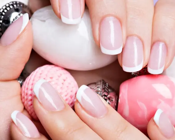 Dłonie z idealnym manicure francuskim, otoczone różowymi i białymi ozdobami.