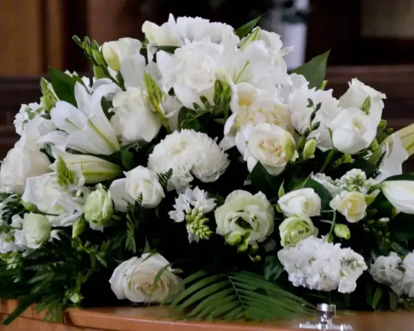 Un arreglo floral blanco sobre un ataúd, con lirios, rosas y otras flores. Estas flores para difuntos simbolizan paz y pureza en el adiós.