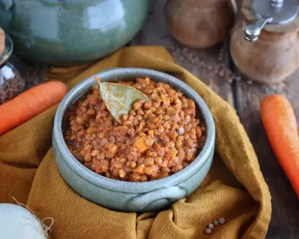 Un invitante ragù di lenticchie, profumato con alloro, pronto per essere gustato. Accanto, carote fresche e cipolla.