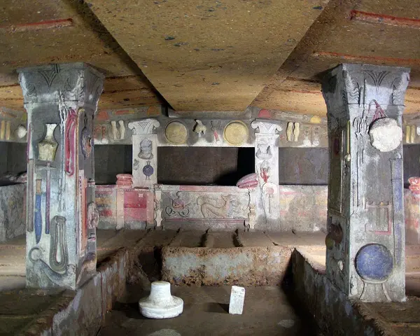 Inside a tomb at the Cerveteri Necropolis, painted columns and walls depict ancient life.