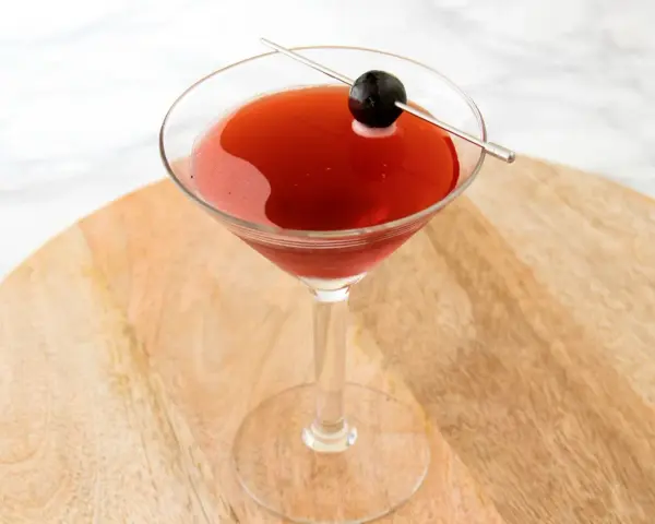 Czerwony drink w kieliszku koktajlowym, ozdobiony oliwką na wykałaczce. Idealny drink San Francisco na letnie wieczory.