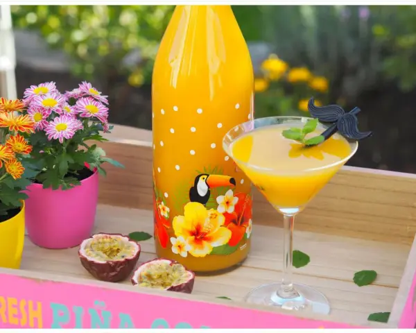 Tropische Früchte und ein leuchtend gelber Drink auf einer rosa Holzschale. Ein ideales Solero Schnaps Rezept ohne Sahne für heiße Tage.