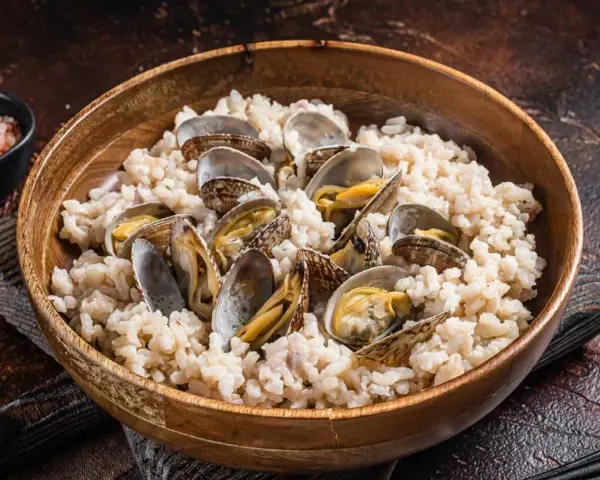 Un tazón de madera lleno de arroz cremoso y almejas frescas, un plato delicioso de arroz con almejas.