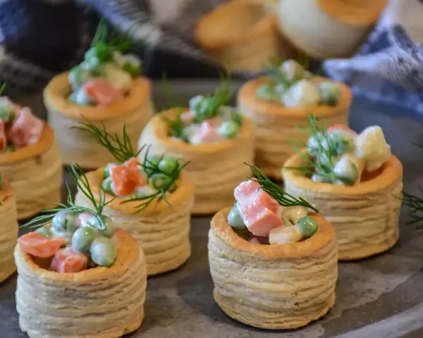 Petits bouchées à la reine, garnies d'une salade crémeuse de petits pois, carottes et jambon, décorées d'aneth. Parfaites pour un apéritif gourmand.