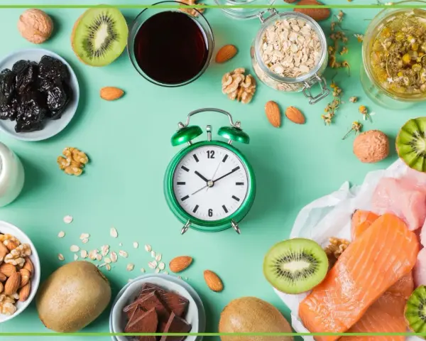 Zielony budzik obok produktów bogatych w tryptofan: łososia, indyka, kiwi, orzechów, migdałów, śliwek, mleka, owsa i czekolady. Zastanawiasz się, po jakim czasie działa tryptofan?