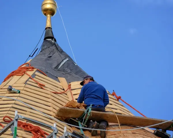 Cieśla dekarz pracuje na dachu, montując drewniane pokrycie.