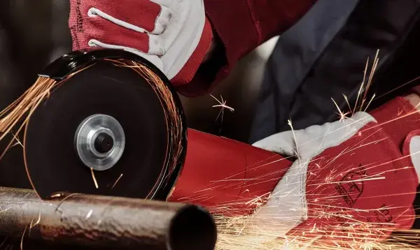 Ręce w czerwonych rękawicach używają szlifierki kątowej, by czym przeciąć metal. Iskry sypią się wokół.