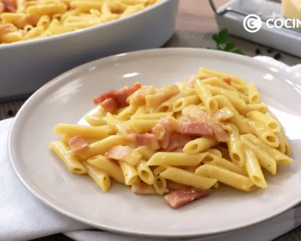 Plato de macarrones a la carbonara cremosos con trozos de panceta. En el fondo, un bol con más pasta y un rallador de queso.