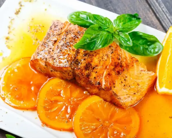 Delicioso salmón a la naranja, servido con rodajas de naranja fresca y hojas de albahaca.