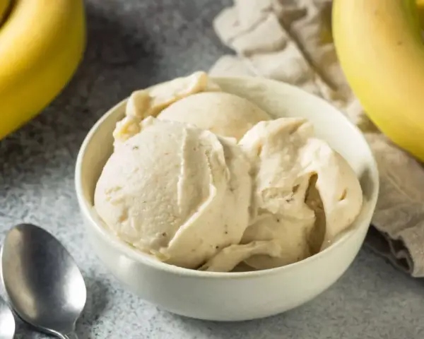 Un cremoso helado de plátano en un tazón blanco, con plátanos amarillos frescos al lado.