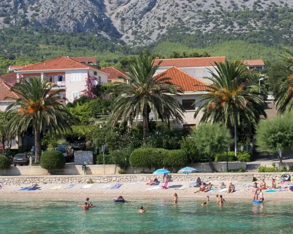 Plaża z palmami, domami i ludźmi kąpiącymi się w morzu.