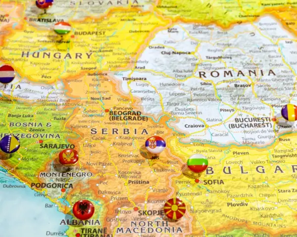 Mapa Europy z zaznaczonymi krajami bałkańskimi, w tym Serbią, Bułgarią i Rumunią, z flagami narodowymi w miejscach stolic.