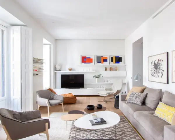 Salón moderno con sofás grises, mesas de centro y arte abstracto. Se aprecia la sutil diferencia entre blanco y blanco roto en paredes y carpintería.
