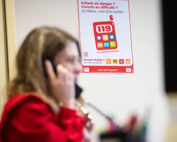 Une femme au téléphone, devant une affiche expliquant le crip signification du numéro 119 pour les enfants en danger.