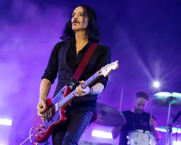 Brian Molko, le chanteur de Placebo, joue de la guitare rouge sur scène, éclairé par des lumières violettes.