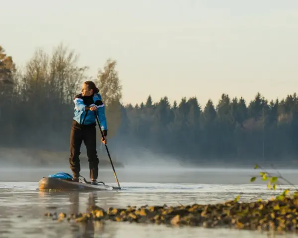 Mann auf Stand Up Paddle, achtet auf die ruhige Wasseroberfläche und die neblige Morgenstimmung.