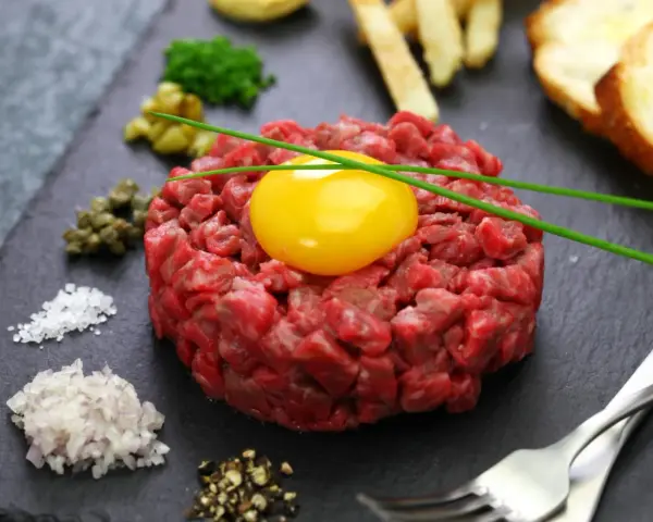 Tartare di manzo fresca e succulenta, con tuorlo d'uovo, capperi, cipolla, sale, pepe e crostini.
