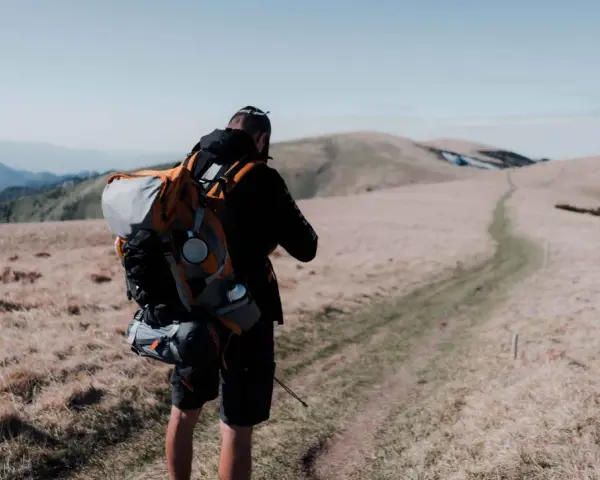 Uomo con zaino da trekking su un sentiero di montagna.
