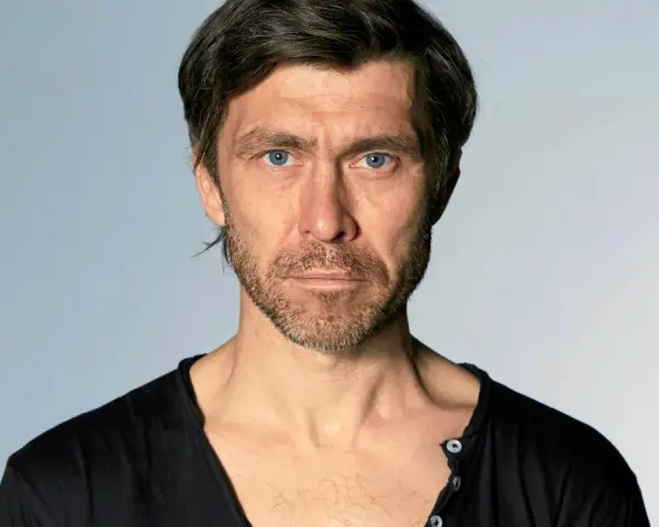 Marcin Czarnik, aktor o intensywnym spojrzeniu i niebieskich oczach, w czarnej koszulce.