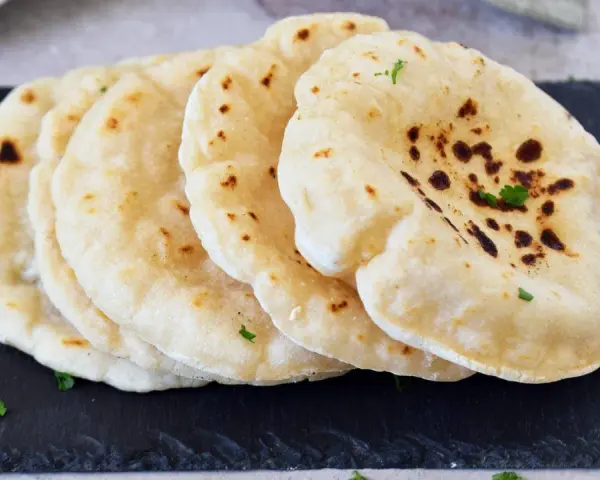 Frisch gebackenes pita brot, leicht gebräunt und mit Petersilie garniert, liegt auf einem dunklen Stein.